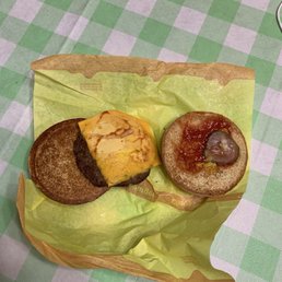 Two breakfast sandwiches with different toppings are placed on yellow paper on a checkered tablecloth.