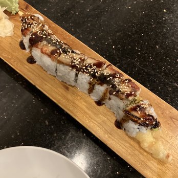 Miso - Dragon Roll - A sushi roll with eel sauce and sesame seeds is presented on a wooden board, accompanied by wasabi and ginger on the side. - Japanese Near Me - Round Rock, Texas