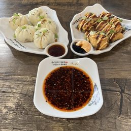 Pad Thai - Three plates of Asian food are displayed on a wooden table: steamed dumplings with soy sauce, fried rolls with sauces, and a bowl of soy-based dipping sauce.
