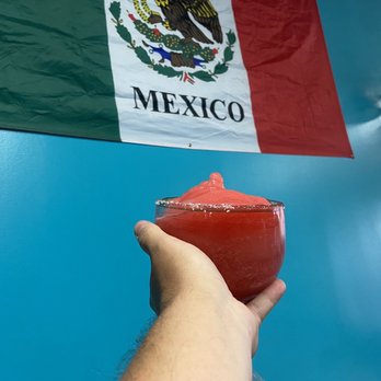La Guacamaya - a hand holding a drink in front of a mexican flag - Mexican Near Me - Clinton, Wisconsin