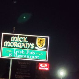 Outside sign - The image shows an illuminated sign for Mick Morgan's Irish Pub & Restaurant at night, featuring the pub's name, a crest, and the words 'Irish Pub & Restaurant.' The sign is set against a dark sky, with some streetlights and additional signs visible in the background.
