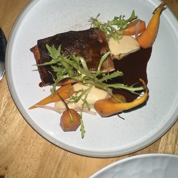 Ariete - SCOTTISH SEA TROUT - A dish with a piece of cooked fish, garnished with greens, served with carrots, a creamy sauce, and a dark sauce on a white plate. - New American Near Me - Miami, Florida