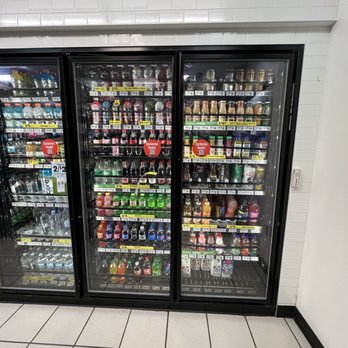 7-Eleven - Drinks - A glass-front refrigerated display case in a convenience store contains bottled beverages, including water, soda, and flavored drinks. - Convenience Stores Near Me - Ithaca, New York