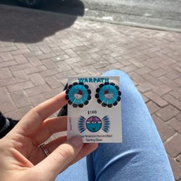Sunface earrings - A person displays a card with turquoise and black flower-shaped earrings, priced at $160, at Warpath Trading Post in Albuquerque, NM.