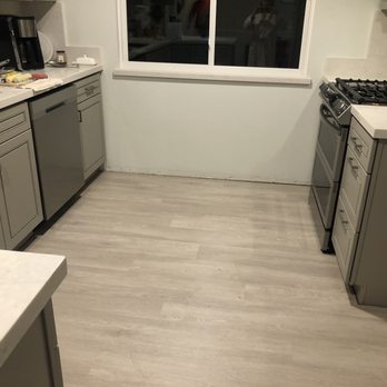 FloorPro - Flooring - A kitchen features gray cabinets, a stove, and a window, with appliances like a coffee maker and toaster on the counter. - Flooring Near Me