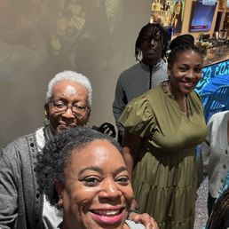 Me and my mother-in-law and my sister-in-law and her son. - Five women and one man are gathered in a bar or restaurant, smiling for a group photo. The background features bar decor and a television screen.