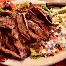 Carne Asada Salad with slices tomatoes and avocados on a bed of lettuce with ranch dressing.