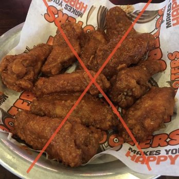 Hooters - Picture from 2019 - A metal basket contains several fried chicken wings on branded paper, with a red cross drawn over the image. - American Near Me - Albuquerque, New Mexico