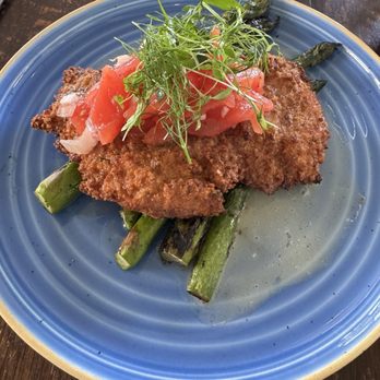 Forge & Vine - Chicken Milanese - A breaded fish fillet, cooked to a golden brown, rests on a bed of grilled asparagus spears. The dish is topped with chopped tomato and a small bunch of microgreens, served on a blue ceramic plate. The presentation emphasizes fresh ingredients and simple plating, with a focus on the crispy fish and vibrant garnishes. - American Near Me - Groton, Massachusetts