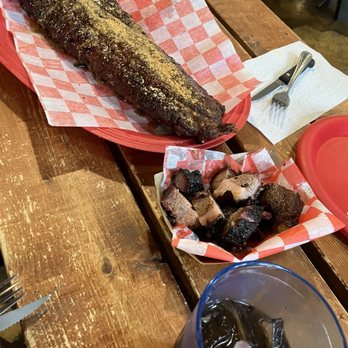 South Moon BBQ - Ribs and burnt ends - A smoked fish on a red tray with checkered paper, chopped smoked pork in a basket, and a glass of soda with ice on a wooden table. - Barbeque Near Me - Hinckley, Illinois