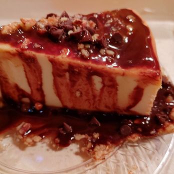 Lazy Cloud Lodge - Cheesecake - A slice of cheesecake with a smooth, creamy texture, topped with chocolate sauce and chopped nuts, served on a clear glass plate. - Bed & Breakfast Near Me - Fontana, Wisconsin