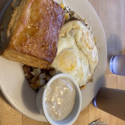 Loco Moco - A breakfast dish featuring a large piece of French toast, two fried eggs, hash browns, and a cup of gravy on a white plate.