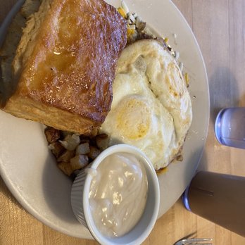 Loco Cafe - Loco Moco with honey biscuit and gravy (on a bed of  hashbrowns) - A breakfast dish featuring a large piece of French toast, two fried eggs, hash browns, and a cup of gravy on a white plate. - Breakfast & Brunch Near Me - Denton, Texas