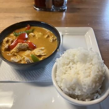 Thai Table - CU1. Panang Curry Dinner - A bowl of Thai curry with red and green peppers and chicken, accompanied by a bowl of white rice, on a white tray at a restaurant. - Thai Near Me - Topeka, Kansas