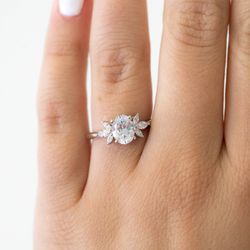 Wilson Diamonds - White gold oval engagement ring with marquise accent stones, featured on hand. This engagement ring is whimsical and romantic.