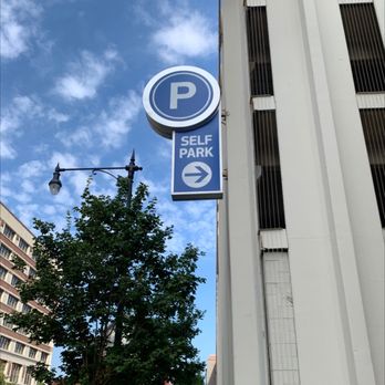 P Self Park - A blue and white parking sign with a 'P' symbol and 'SELF PARK' text, featuring a right-pointing arrow, mounted on a building exterior. - Parking Near Me
