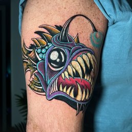 Did the hammerhead a few weeks ago. Angler fish yesterday. Both came out perfect. Kevin did excellent work on both pieces. Highly recommend - A vibrant tattoo of a fish with large eyes, sharp teeth, and intricate details covers the upper arm, showcasing realism and bold colors.