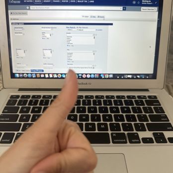 Quality Plus Computer - A person is holding up their hand with a thumbs-up gesture in front of a MacBook Air laptop. The laptop screen displays a real estate search webpage with filters for address, city, and other criteria. The image captures the keyboard and part of the laptop's screen, indicating a positive or approving gesture related to the webpage content. - IT Services & Computer Repair Near Me - Chino Hills, California
