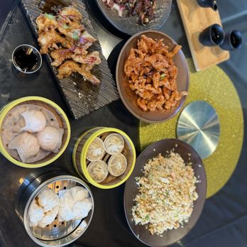 Colette - Assorted Asian cuisine dishes are displayed on a black table, including dumplings, fried rice, stir-fried beef, and fried chicken, with tea and condiments. - Breakfast & Brunch Near Me - Pasadena, California
