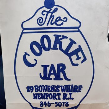 The Cookie Jar - a sign for the cookie jar - The image shows a white paper bag with a blue printed logo and text. The logo features a stylized jar with a lid and a small round handle on top. Inside the jar outline, the words "The Cookie Jar" are written, with "The" in cursive and "Cookie Jar" in bold, uppercase letters. Below the logo, the address "29 Bowens Wharf, Newport, RI" and the phone number "846-5078" are printed. The bag appears to be crumpled and is likely used for carrying baked goods from The Cookie Jar in Newport, RI. - Bakeries Near Me - Newport, Rhode Island
