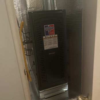 Evolution Heating And Air Conditioning - Heater - A black furnace unit is installed in a small closet with metallic insulation panels on the walls, connected to yellow and black pipes. - Heating & Air Conditioning/HVAC Near Me - Fullerton, California