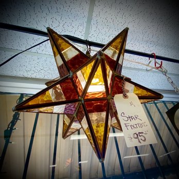 Bougie Bazaar - Always new amazing things to see at this store !! - A star-shaped decorative fixture made of multiple glass panels in amber and red hues is hanging from a ceiling grid. The fixture is attached with a chain and has a handwritten price tag reading '$95' labeled 'Star Fixture.' The ceiling consists of white acoustic tiles, and the fixture is displayed in an indoor setting, likely a store or showroom. - Antiques Near Me - Pasadena, California