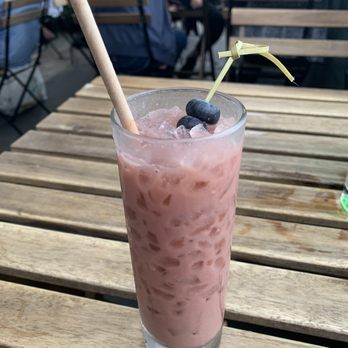 The Binc - A blueberry cocktail - A tall glass of pink blueberry cocktail with ice, garnished with blueberries and a straw, on a wooden outdoor table at a restaurant or bar. - Cocktail Bars Near Me - Brooklyn, New York