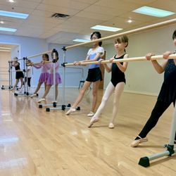 Children standing at the ballet barre with pointed toes - smiling