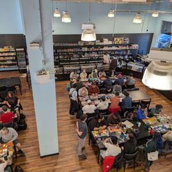 Cardboard Classic Games - Groups of people are sitting at tables playing trading card games