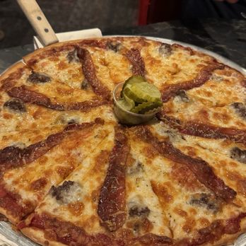 Leonardo's - Bacon Cheeseburger Pizza - A pizza topped with bacon, cheese, and mushrooms, served on a metal tray with a small container of pickles in the center. - Pizza Near Me - Cedar Rapids, Iowa
