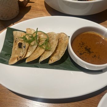 SŌW Plated - Kimchi dumplings - Four dumplings are arranged on a white plate with a small bowl of dipping sauce, garnished with green onion. - New American Near Me - Upper Arlington, Ohio