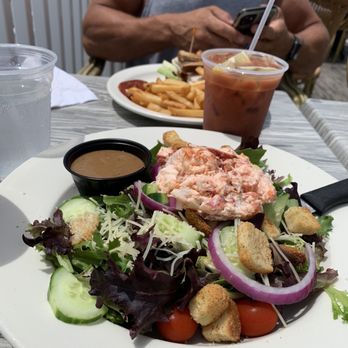 The Point - Mixed greens salad with lobster, Bloody Mary's, and turkey BLT for lunch! - A seafood salad with lettuce, cucumbers, cherry tomatoes, red onions, croutons, and a pink seafood mixture, served with a small container of dressing. - American Near Me - Marshfield, Massachusetts