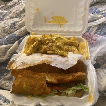 This is SEAFOOD - Whiting Po'Boy Combo - A seafood takeout meal in a foam container includes fried fish, seasoned fries, and pasta with yellow sauce and black pepper, placed on a bed of lettuce. - Seafood Near Me - District Heights, Maryland