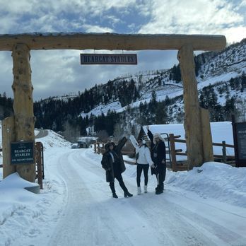 Bearcat Stables - Three individuals pose under a wooden arch with a sign reading 'Bearcat Stables' in a snowy mountain landscape, with snow-covered slopes and trees in the background. - Horseback Riding Near Me - Edwards, Colorado