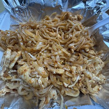 Thai Kitchen - Very spicy Steamed Noodles - A serving of stir-fried noodles with pieces of chicken, bean sprouts, and sauce is presented on crumpled aluminum foil. The noodles appear coated in a savory sauce, and the dish includes cooked chicken chunks and bean sprouts. A white plastic fork is partially visible on the right side of the image. The food is placed on a foam container, suggesting takeout or casual dining. - Thai Near Me - Independence, Missouri