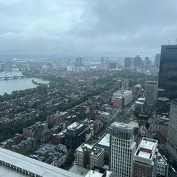 A high-angle view of a city with numerous buildings, a river, and a bridge, under cloudy weather, taken from a tall building.