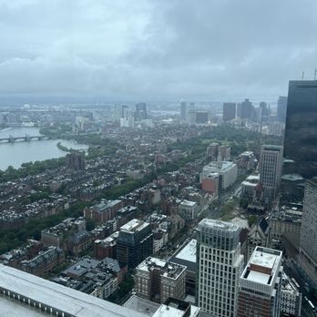 View Boston - A high-angle view of a city with numerous buildings, a river, and a bridge, under cloudy weather, taken from a tall building. - Observatories Near Me - Boston, Massachusetts