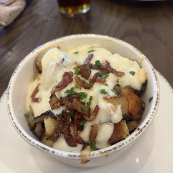 First Watch - Million Dollar Potatoes - A bowl of loaded potatoes with melted cheese, crispy bacon bits, and chopped chives, served on a white plate at a restaurant. - Breakfast & Brunch Near Me - Stuart, Florida