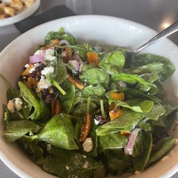 Butternut Squash & Spinach Salad - A spinach and butternut squash salad with crumbled cheese, nuts, and red onions served in a white bowl at a restaurant.