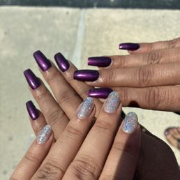 One hand with Holographic gel manicure on real nails, shimmery deep purple acrylic manicure on another pair of hands. One hand with Holographic gel manicure on real nails, shimmery deep purple acrylic manicure on another pair of hands.