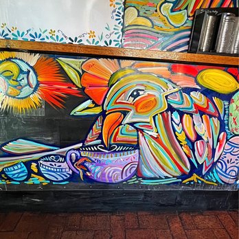 Blackbird Coffee House - Counter - A mural featuring a toucan with multicolored feathers, a cup, and abstract shapes is painted on a wall inside a cafe, with a brick floor. - Coffee & Tea Near Me - Albuquerque, New Mexico