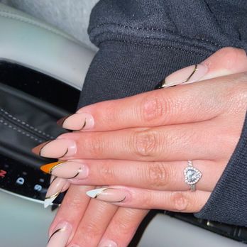 AVA Nail Bar - A person's hands with manicured nails featuring a French tip design with orange accents, wearing a diamond ring, resting on a car's gear shift. - Nail Salons Near Me - Schaumburg, Illinois