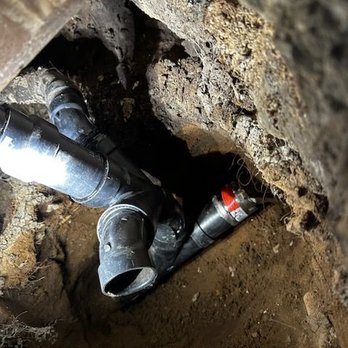 Arsenal Plumbing and Drains - A close-up view of black plastic drain pipes (likely PVC or ABS) connected with fittings in a tight, dark hole... - Plumbing Near Me Arsenal Plumbing and Drains - A close-up view of black plastic drain pipes (likely PVC or ABS) connected with fittings in a tight, dark hole... - Plumbing Near Me