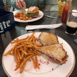 Took bite of Ruben and fries but didn't have dip til my husband gave me his! - A plate with a toasted sandwich, French fries, and a small side of coleslaw on a black metal table at a restaurant.