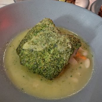 Runner Up - Pollock - A fish fillet with a green herb crust is presented in a shallow bowl with a light broth and some vegetables underneath. - French Near Me - Brooklyn, New York