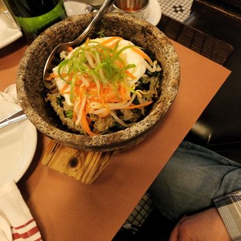 The Smith - A stone bowl of bibimbap with vegetables, a poached egg, and rice, accompanied by side dishes and condiments on a restaurant table. - New American Near Me - Washington, DC, District of Columbia