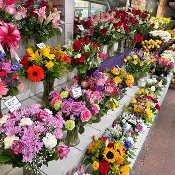 Conroy's Flowers - Vibrant flower arrangements on display in an open-air market, featuring roses, lilies, and sunflowers with festive ribbons and a balloon. - Florists Near Me - Torrance, California Conroy's Flowers - Vibrant flower arrangements on display in an open-air market, featuring roses, lilies, and sunflowers with festive ribbons and a balloon. - Florists Near Me - Torrance, California