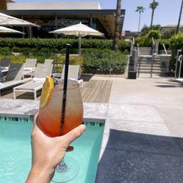 a person holding a cocktail in front of a swimming pool a person holding a cocktail in front of a swimming pool