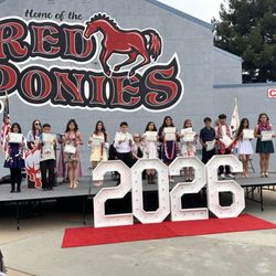 John E Steinbeck Elementary School - Boys and girls holding diplomas in front of a Red Ponies mural