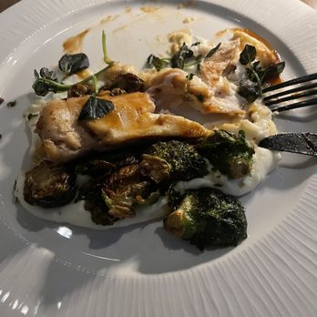 The Compass - Chicken dish. I forgot to take the picture before we started eating - A white plate holds a partially eaten meal consisting of roasted chicken, Brussels sprouts, and microgreens. The dish appears to be served at a restaurant, with some sauce and food remnants visible on the plate. The presentation includes microgreens as garnish, and the plate is placed on a wooden table. - American Near Me - Phoenix, Arizona